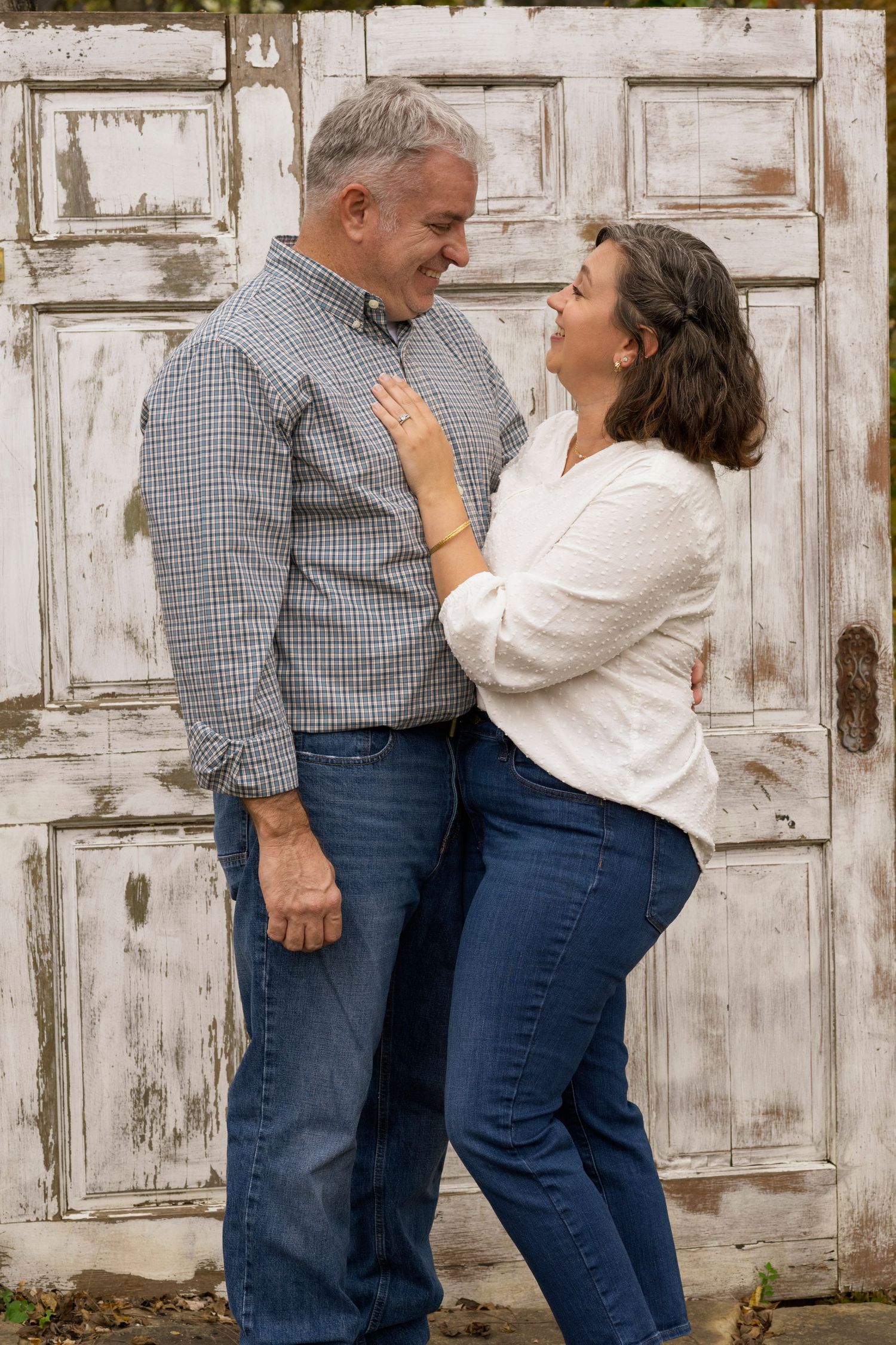 A couple shares playful moments against a rustic white door background in a casual photo series.