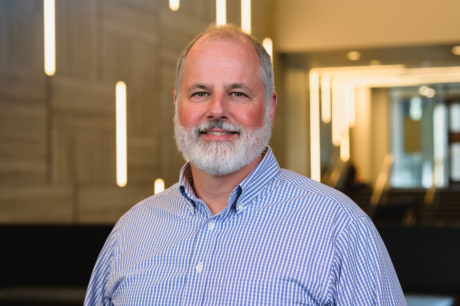 Business portrait of person in striped button-down shirt against modern office setting.