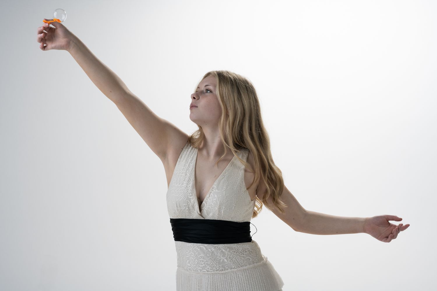 Person in white dress with black waistband striking graceful pose against white background.