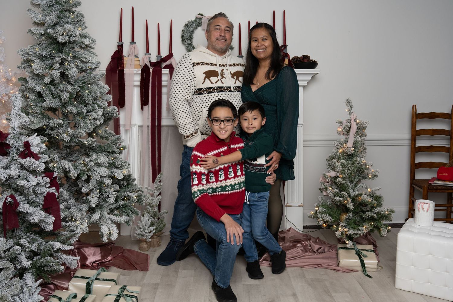 Family holiday portrait with Christmas trees and decorative backdrop.