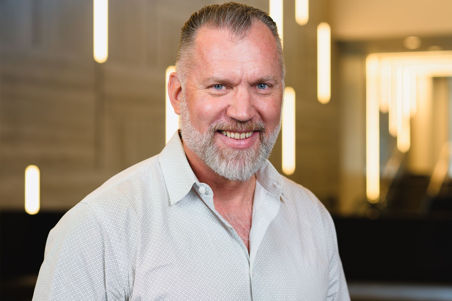 Professional portrait of person in white collared shirt against modern office lighting.
