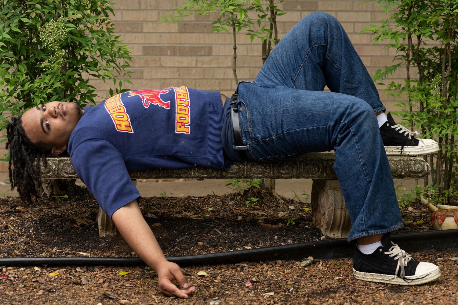 Someone lying on a brick ledge wearing blue jeans and a navy sweatshirt.