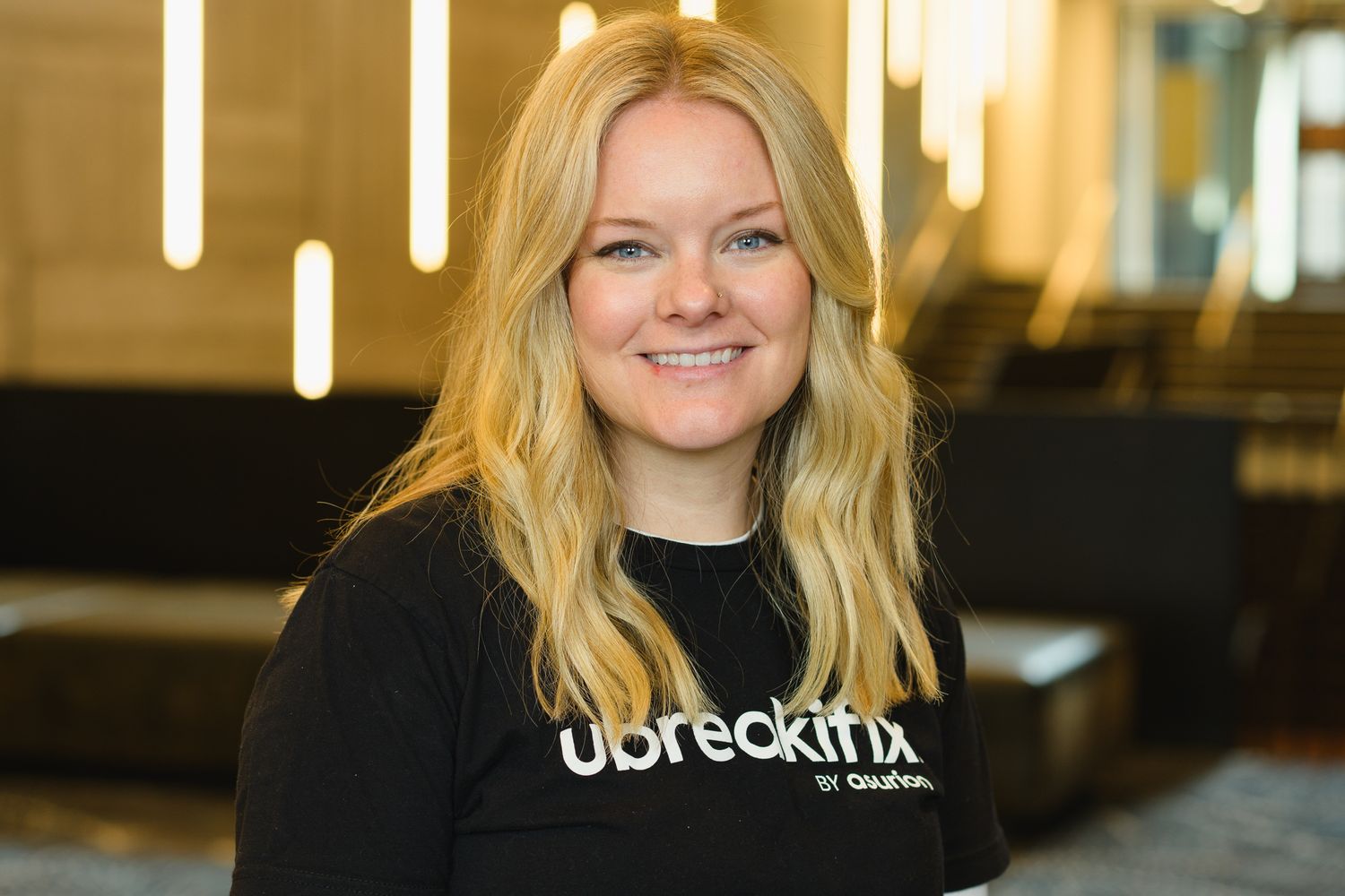 Person in dark clothing with company branding smiling warmly at the camera.