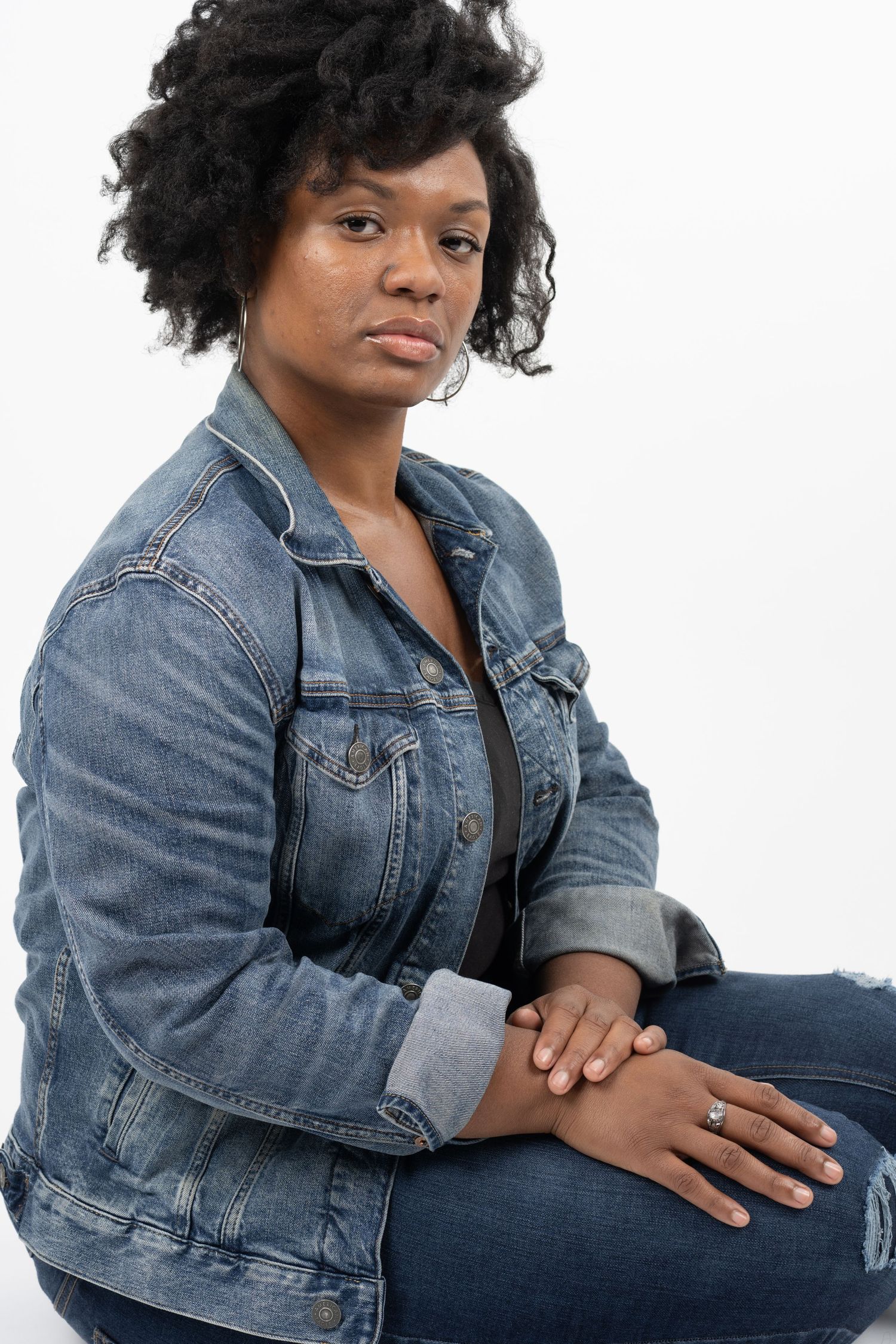 Model in denim jacket poses confidently against white background in portrait series.
