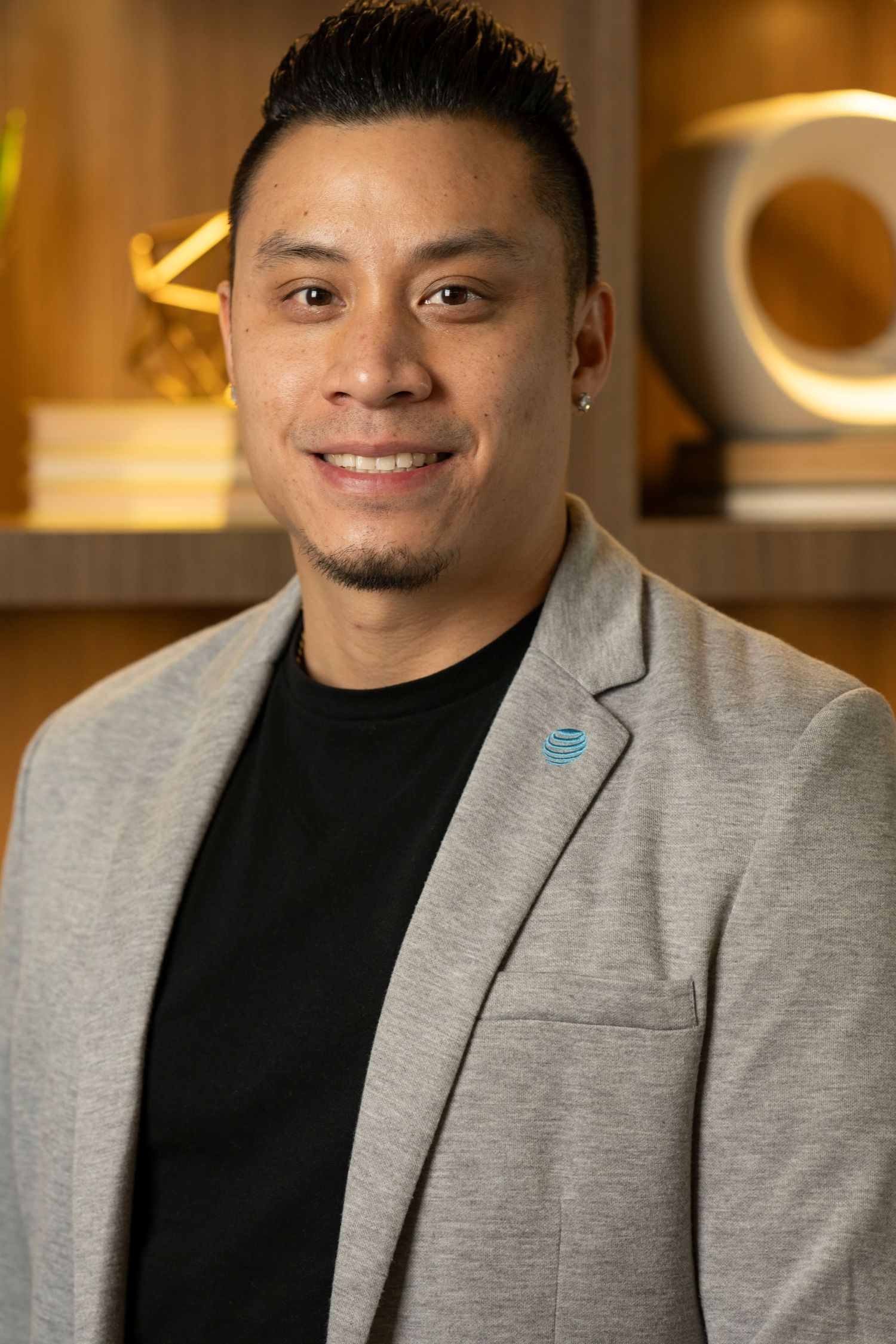 Professional portrait of person in black turtleneck and grey blazer with warm office lighting.