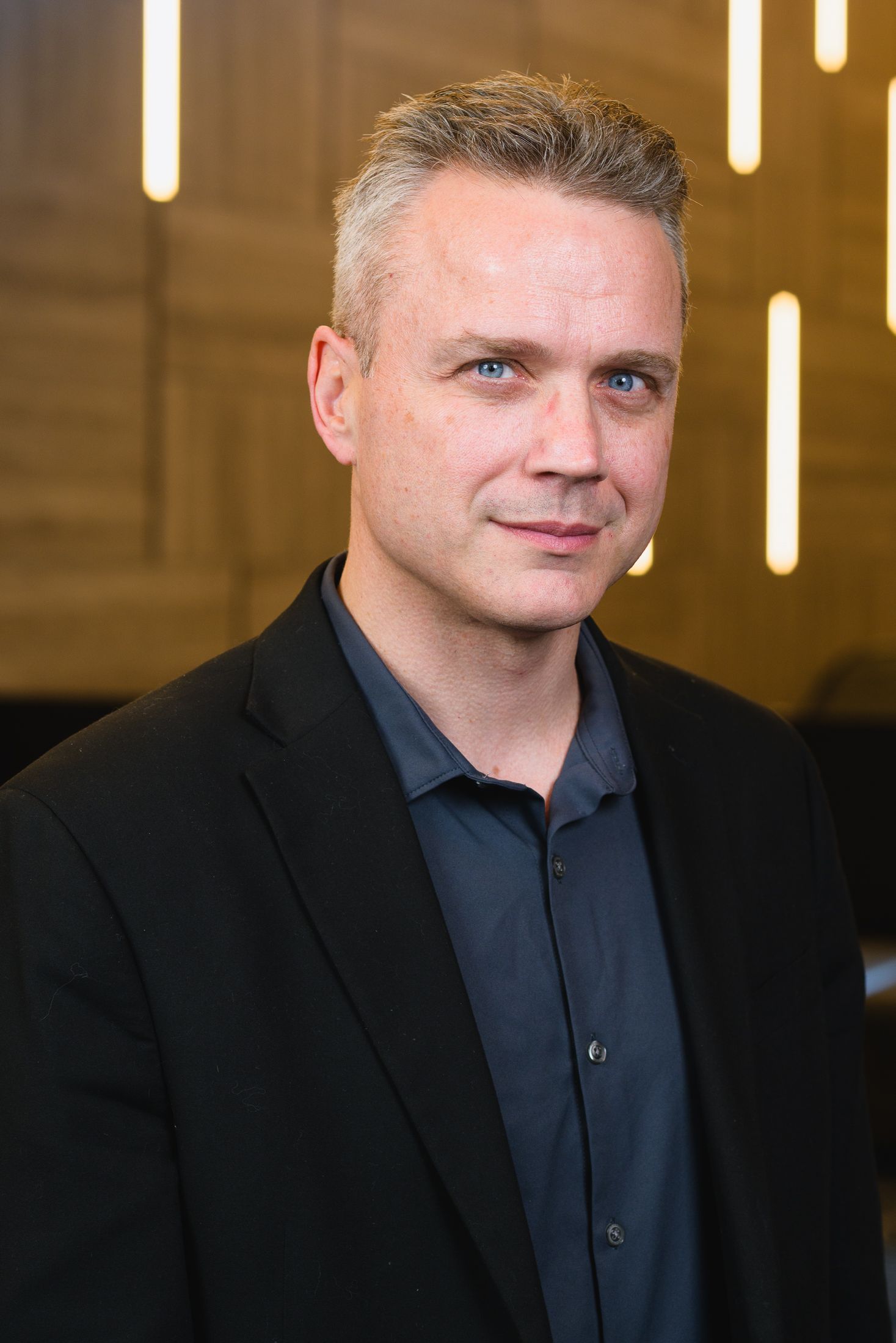 Corporate headshot featuring a person in dark business attire against vertical lighting fixtures.