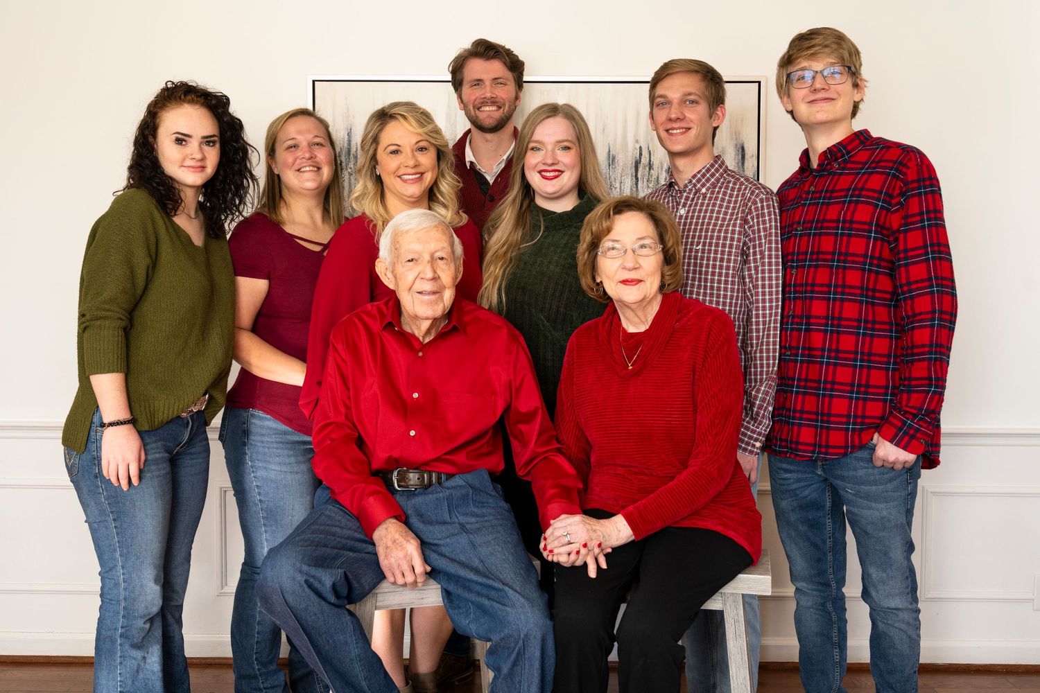 Family group photo with members wearing coordinated red and casual attire against white wall.