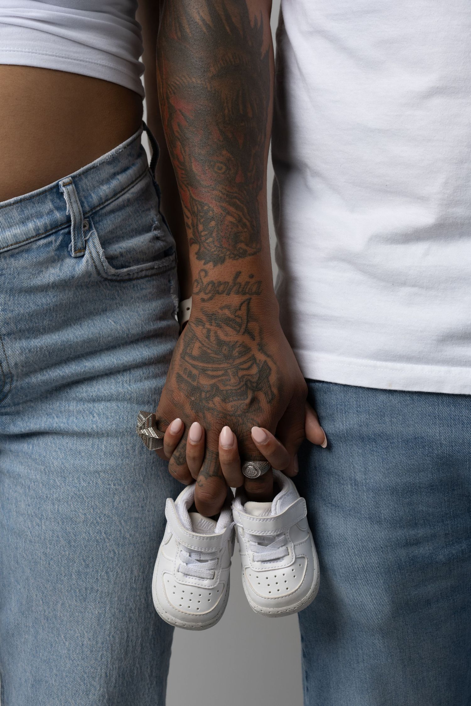 Hands holding small white baby shoes against denim background.