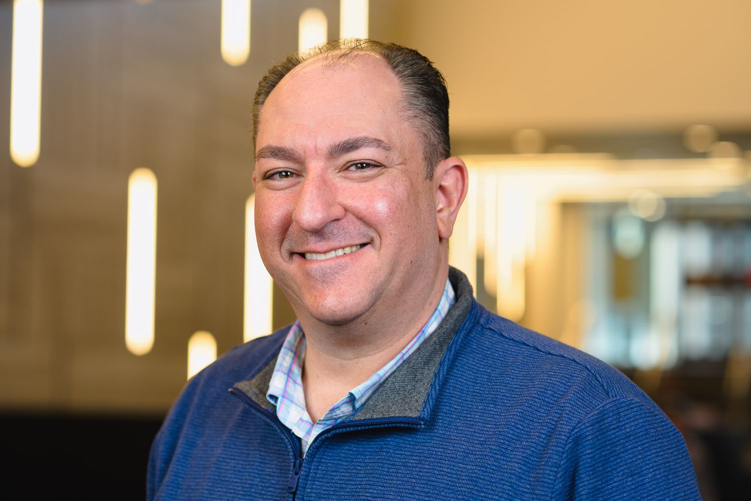 Professional in blue quarter-zip sweater smiling in corporate environment.