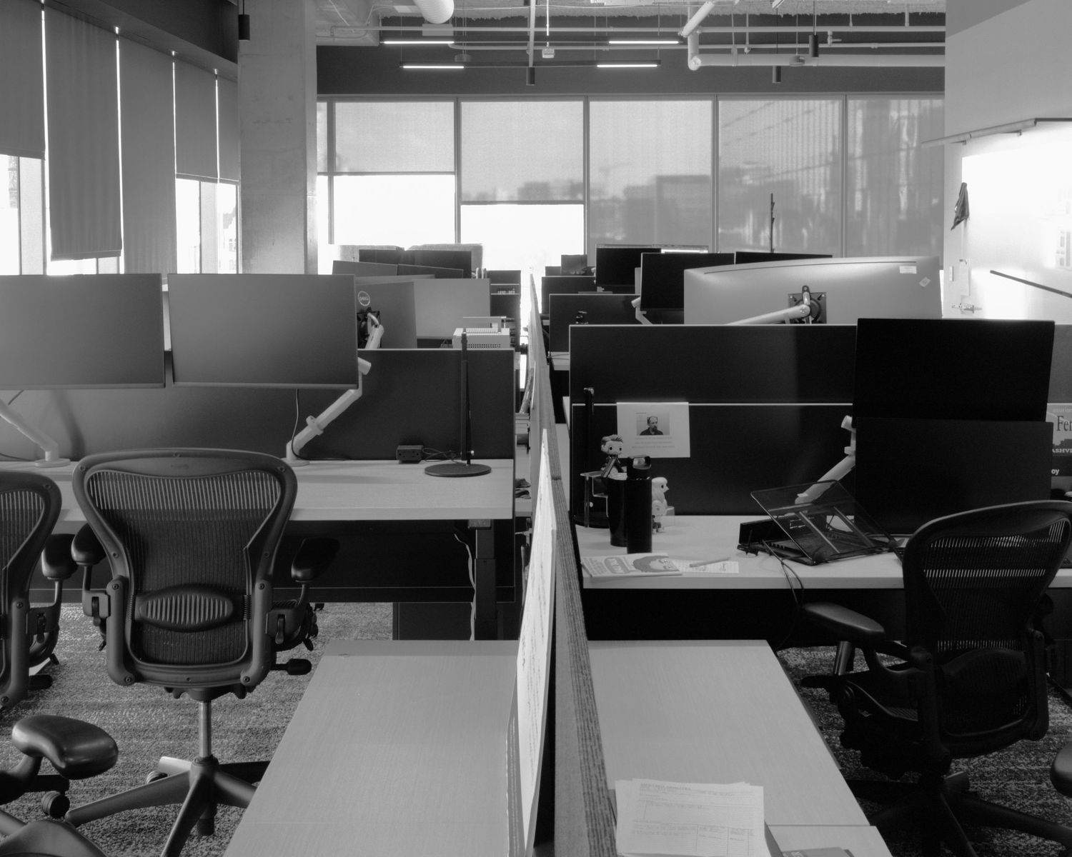 Empty modern office space with white desks and chairs under fluorescent lighting.