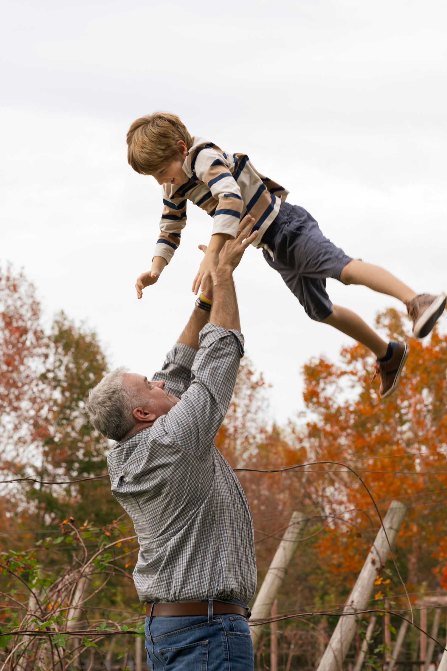 Joyful outdoor scene of someone lifting a child up into the autumn air.