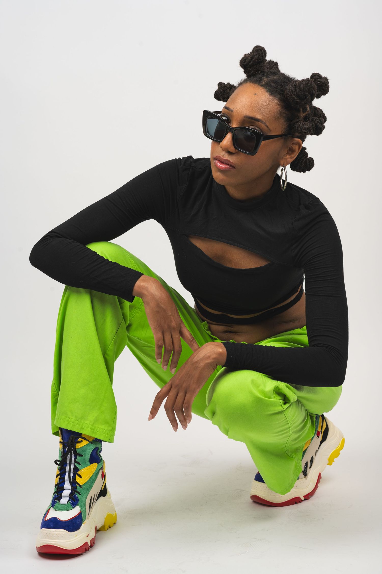 Dancer in black top and neon pants striking low poses with colorful sneakers.