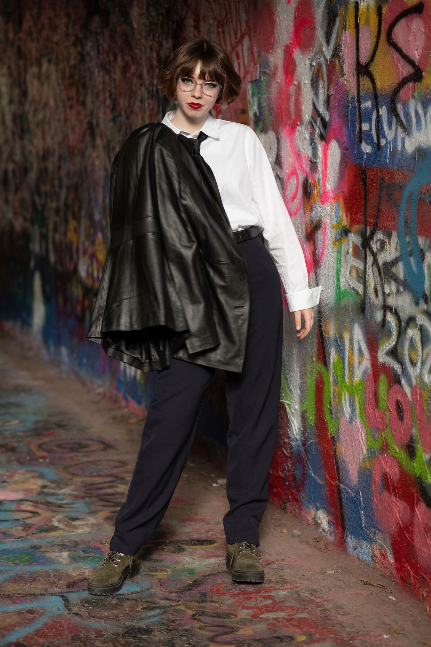 Figure in black and white outfit stands against colorful urban graffiti backdrop in artistic photoshoot.