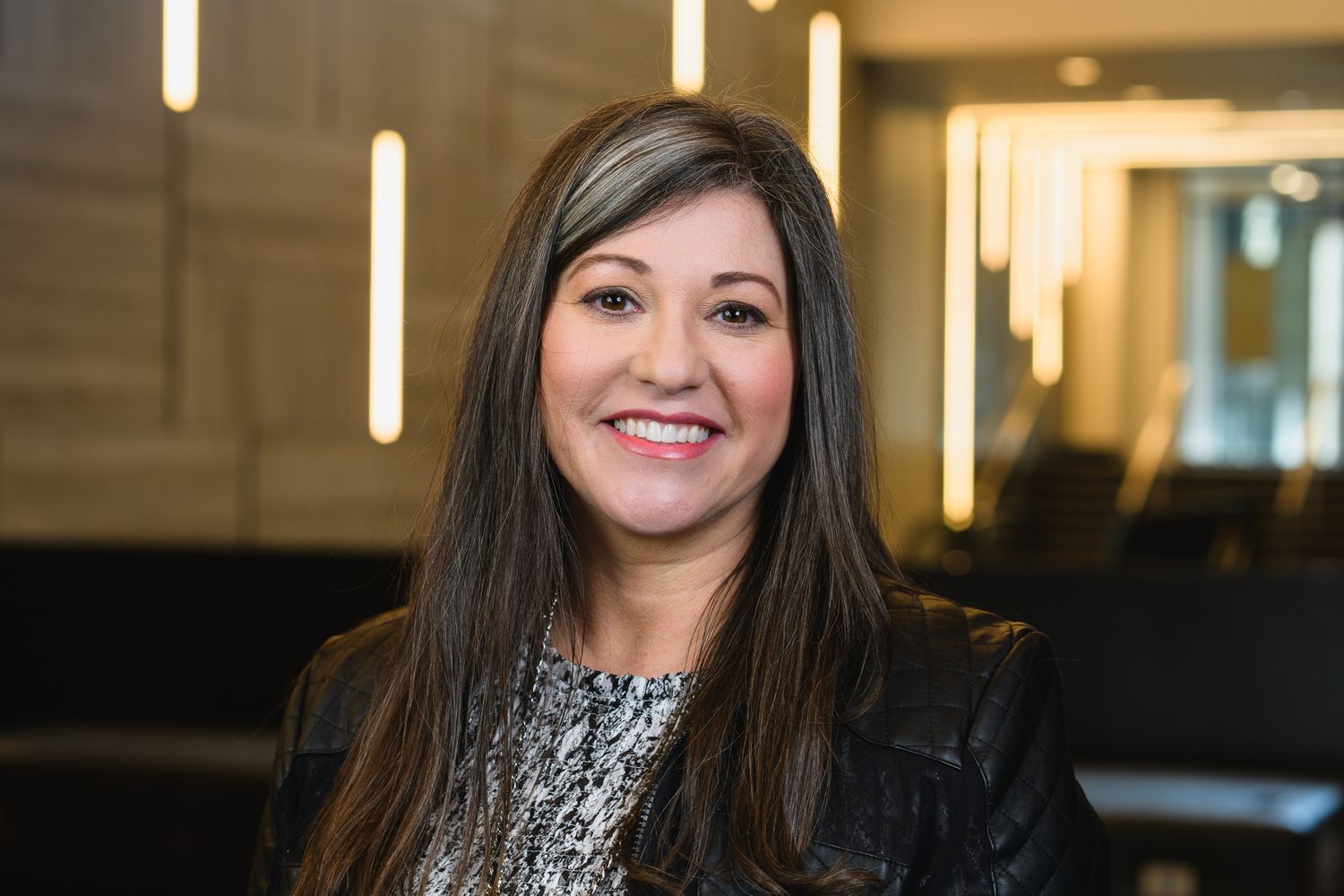 Professional headshot of person in patterned top against modern office background.