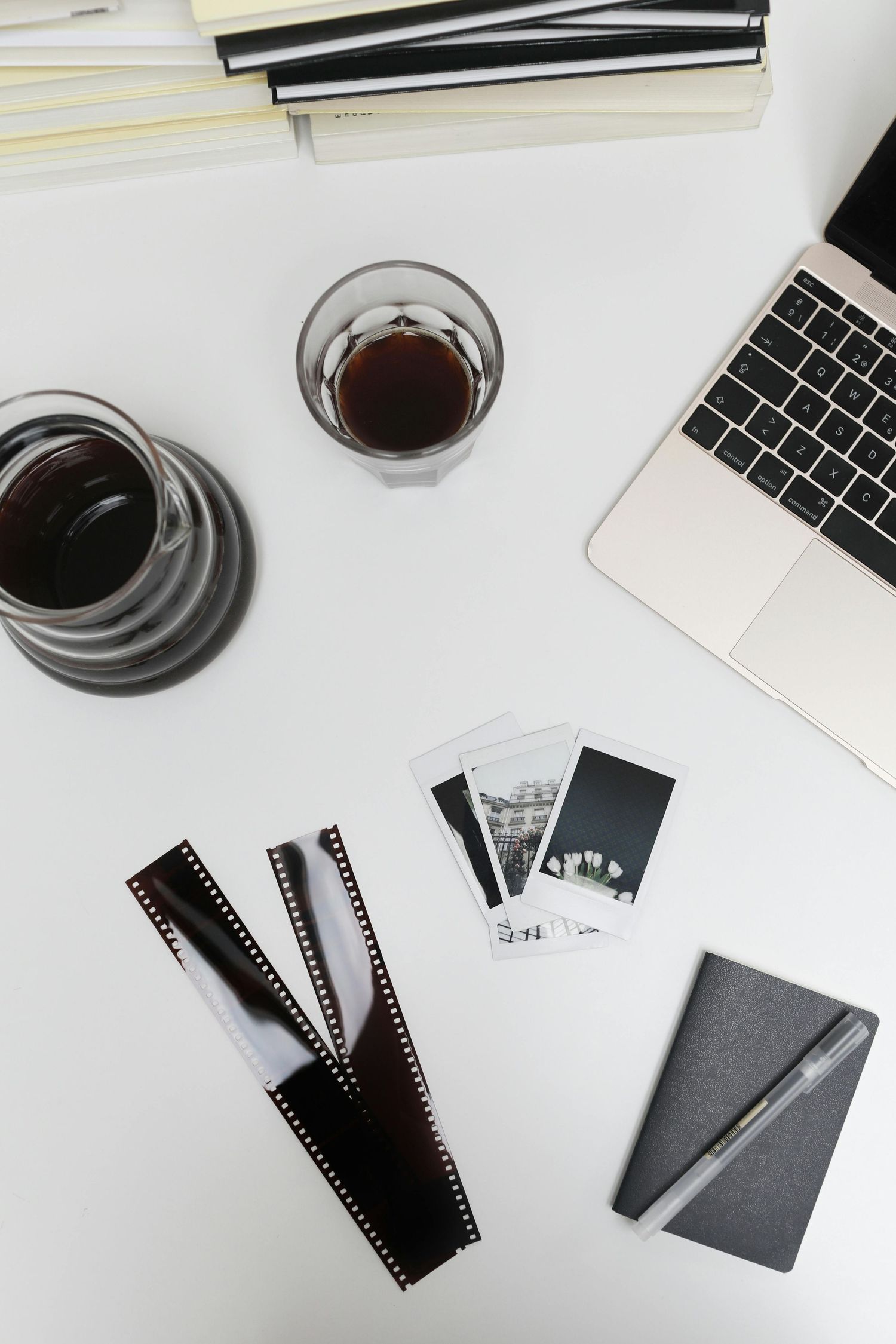 Film negatives and coffee cup arranged on white desk with laptop keyboard and notebook in minimalist workspace setup.