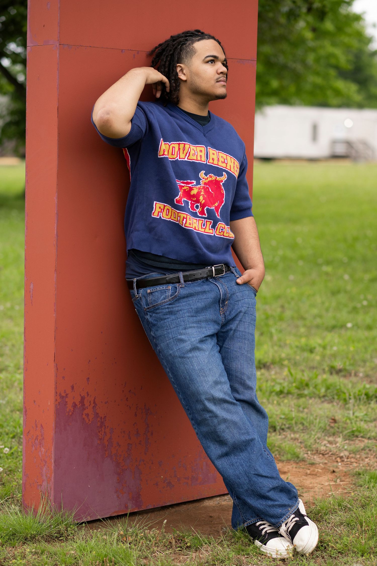 A person in a navy Howard Bison t-shirt and jeans leans against a red post in a grassy outdoor setting.