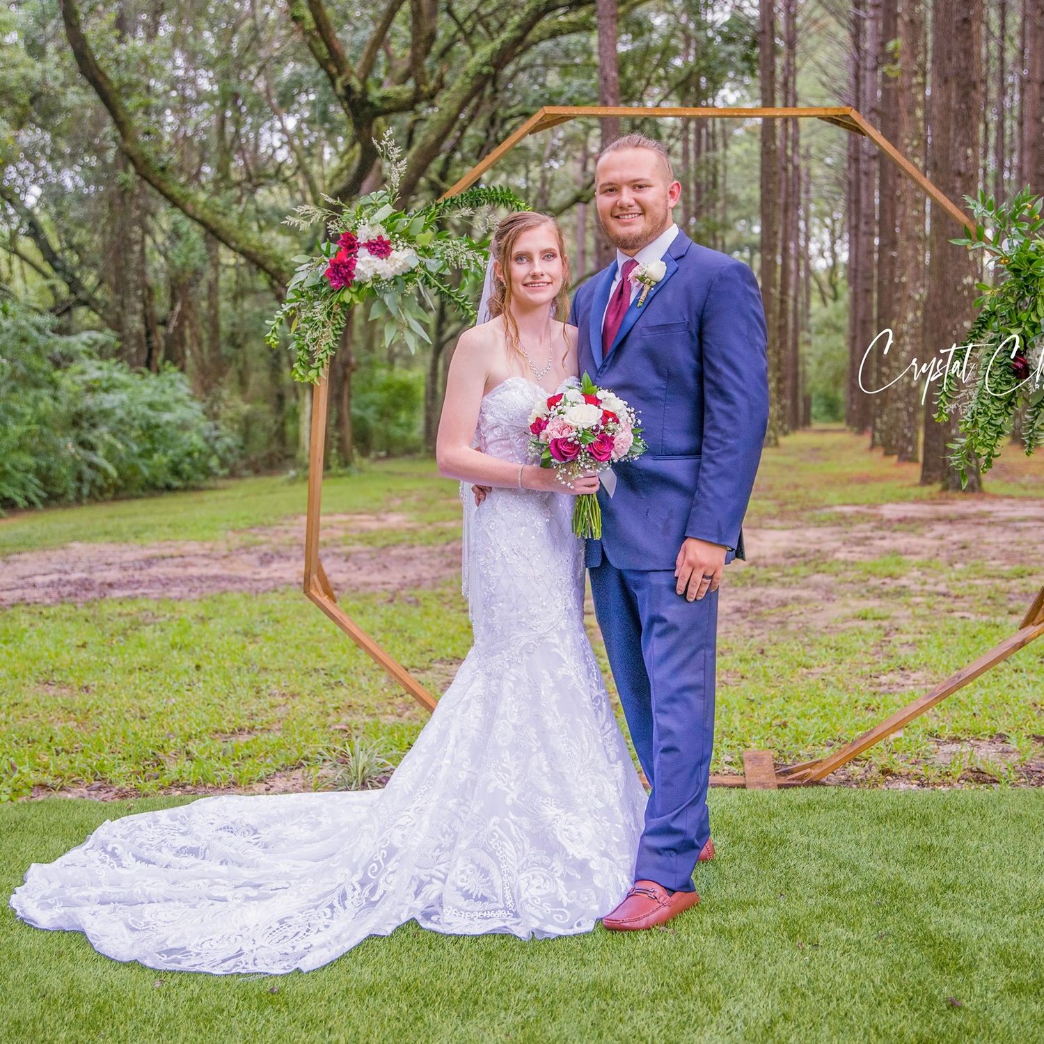 Wedding couple poses in a romantic outdoor forest setting with heart-shaped frame.