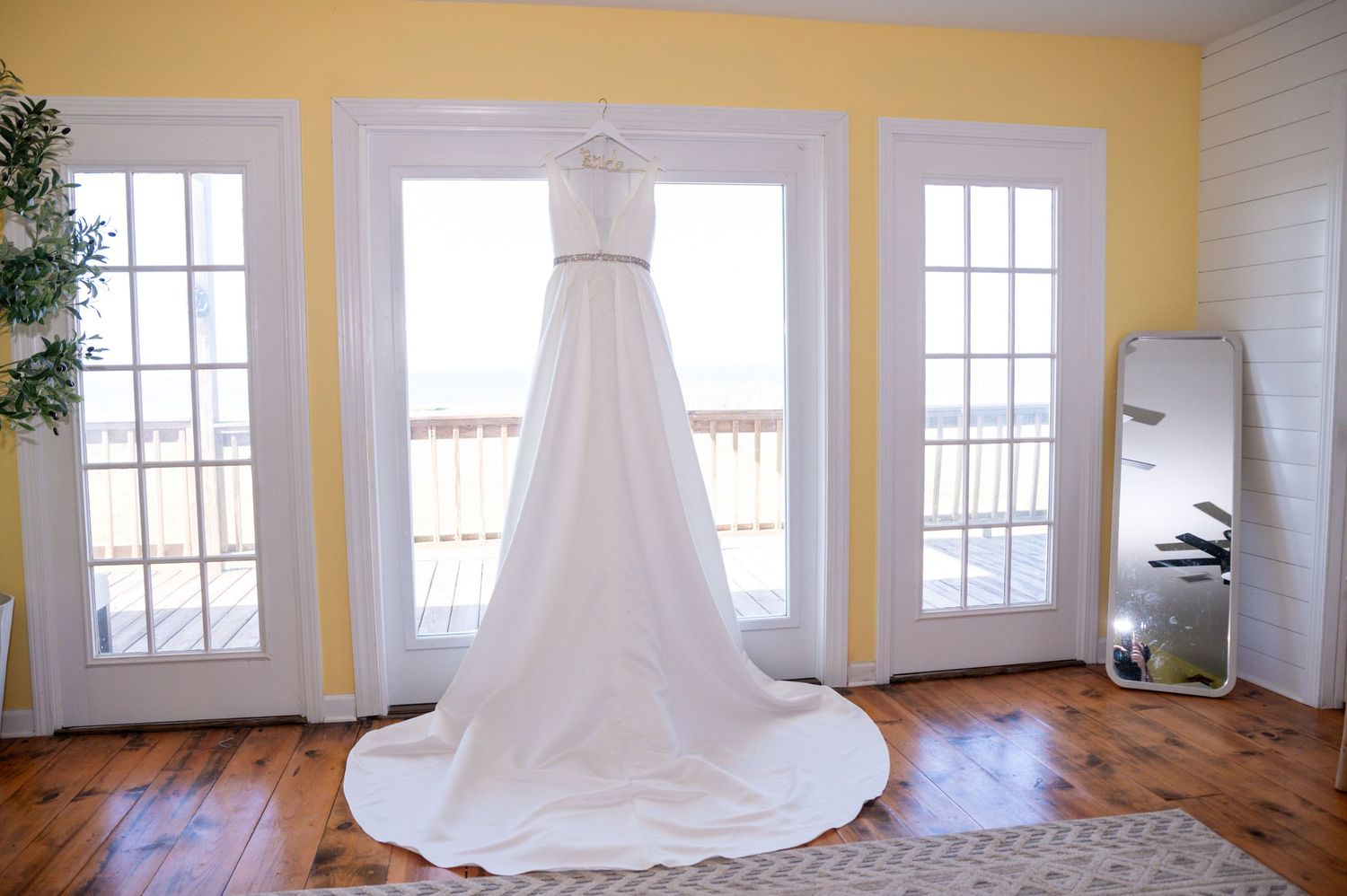 Empty wedding venue room with yellow walls and white hanging dress by windows.