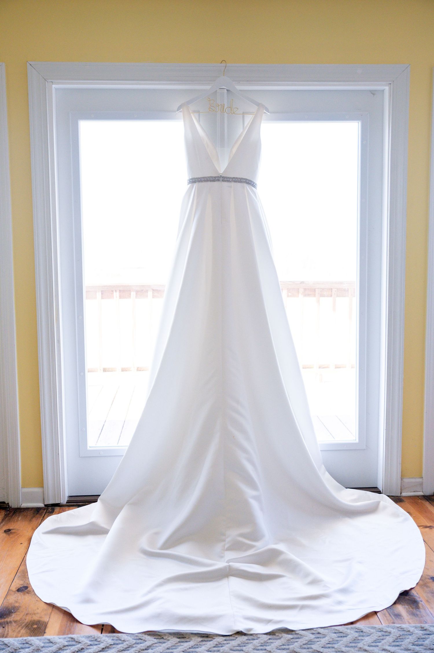 Elegant white wedding dress displayed in front of bright windows.