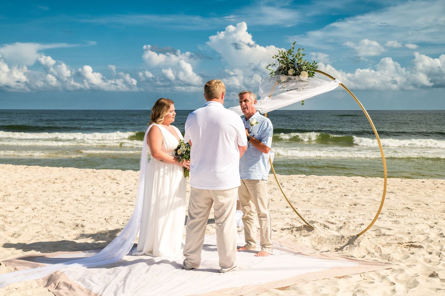 Beach wedding ceremony setup with white chairs and ocean backdrop on a sunny day.