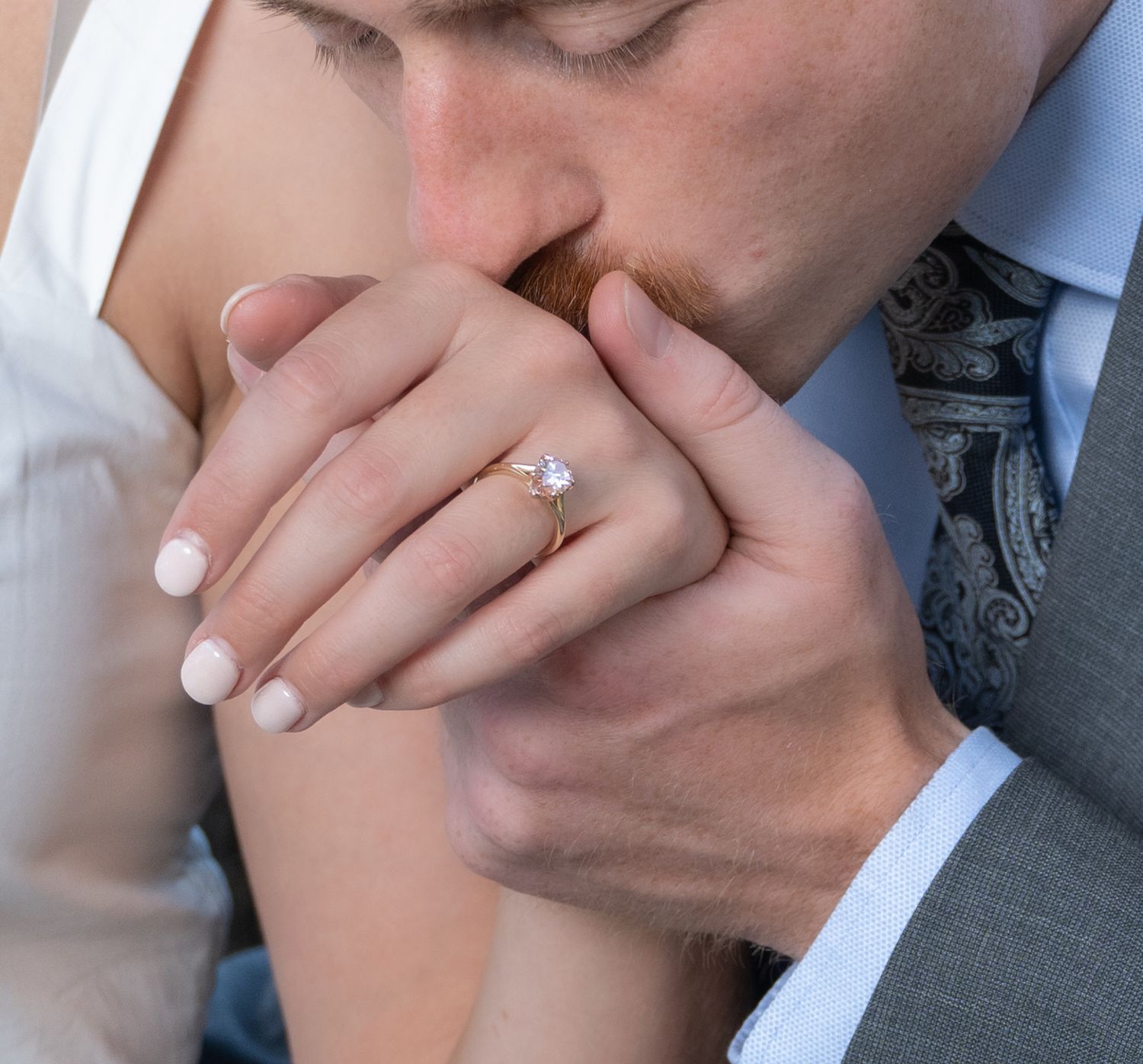 Close-up of engagement ring with white manicured nails against formal attire.