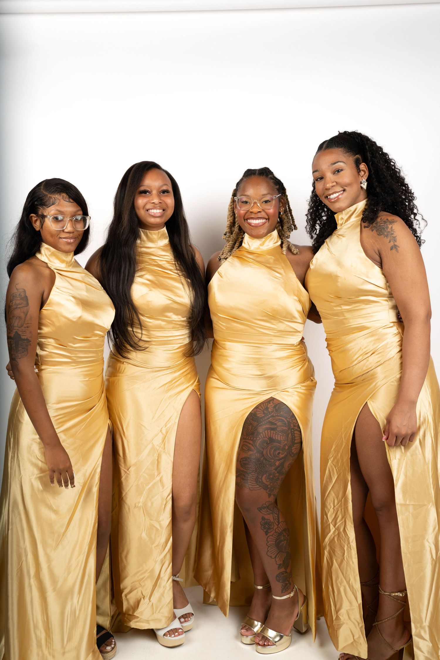 A group of people wearing matching gold satin dresses pose together in a line against a white background.