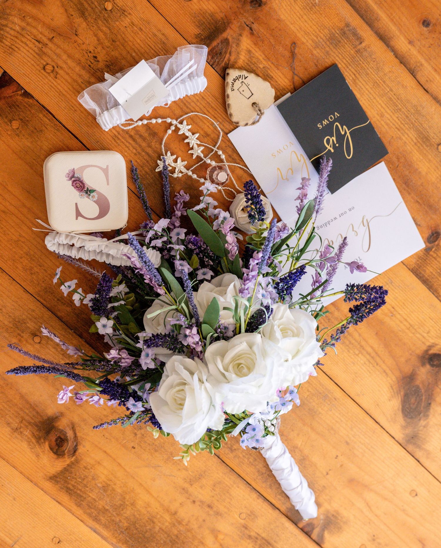 Wedding bouquet with white roses and purple flowers arranged on rustic wooden surface.