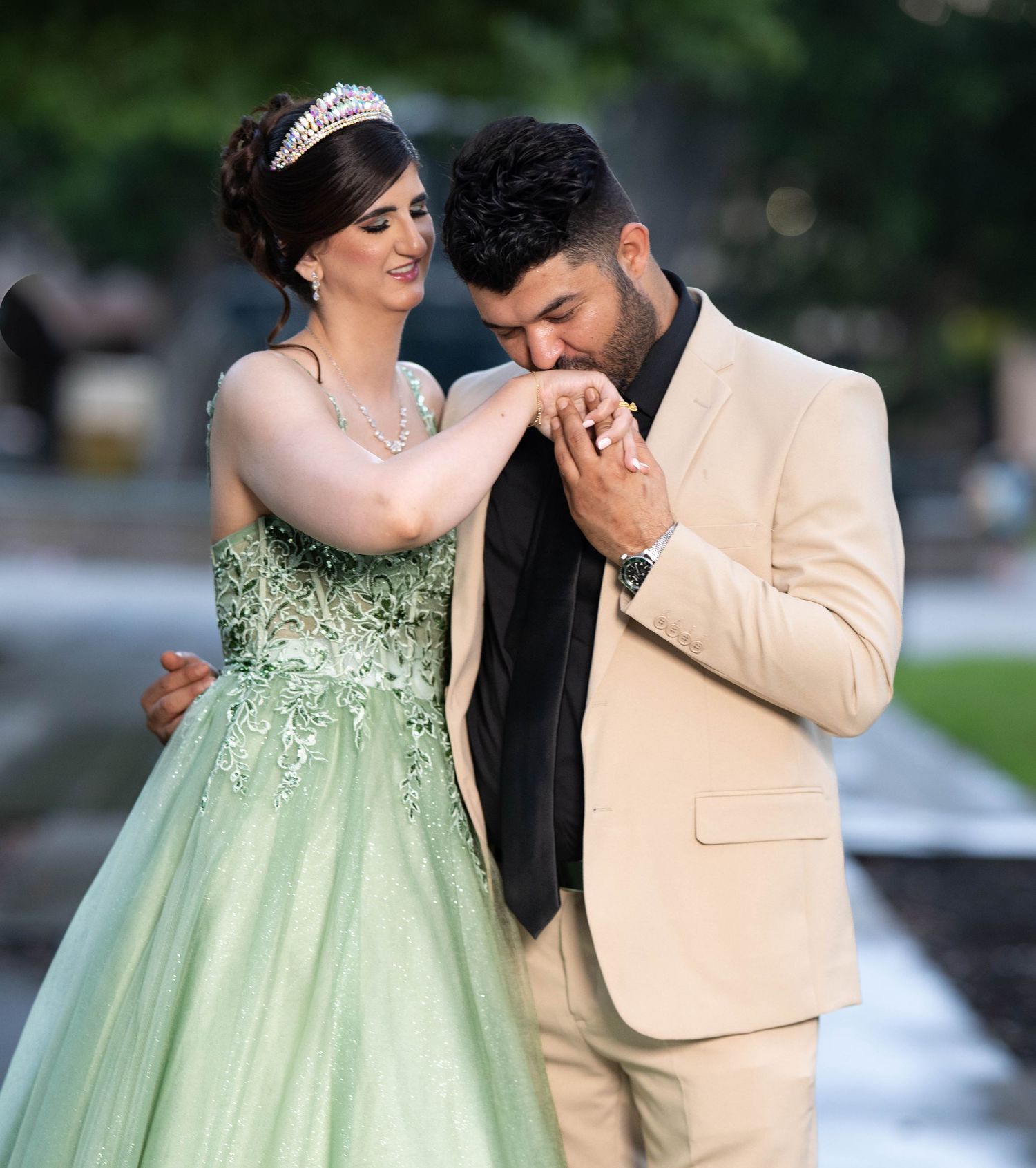 A couple shares a romantic moment in an outdoor setting, with the person wearing a mint green formal gown.