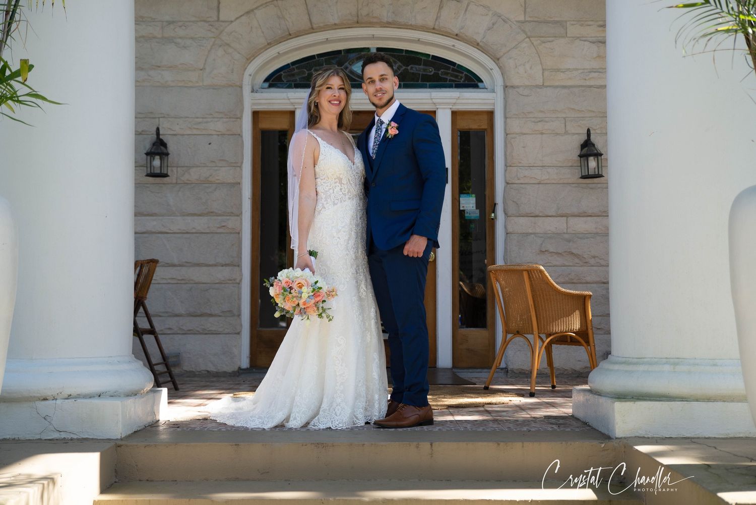 Elegant wedding ceremony at a stone columned entrance with white decor and floral arrangements.