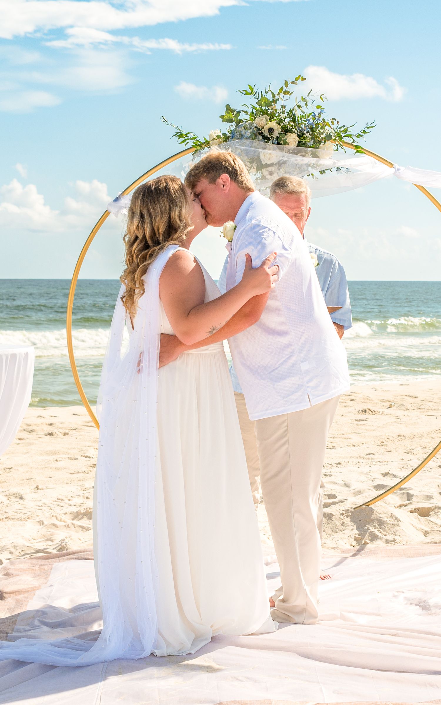 Beach wedding ceremony photos with a golden arch and white fabric against the ocean backdrop.