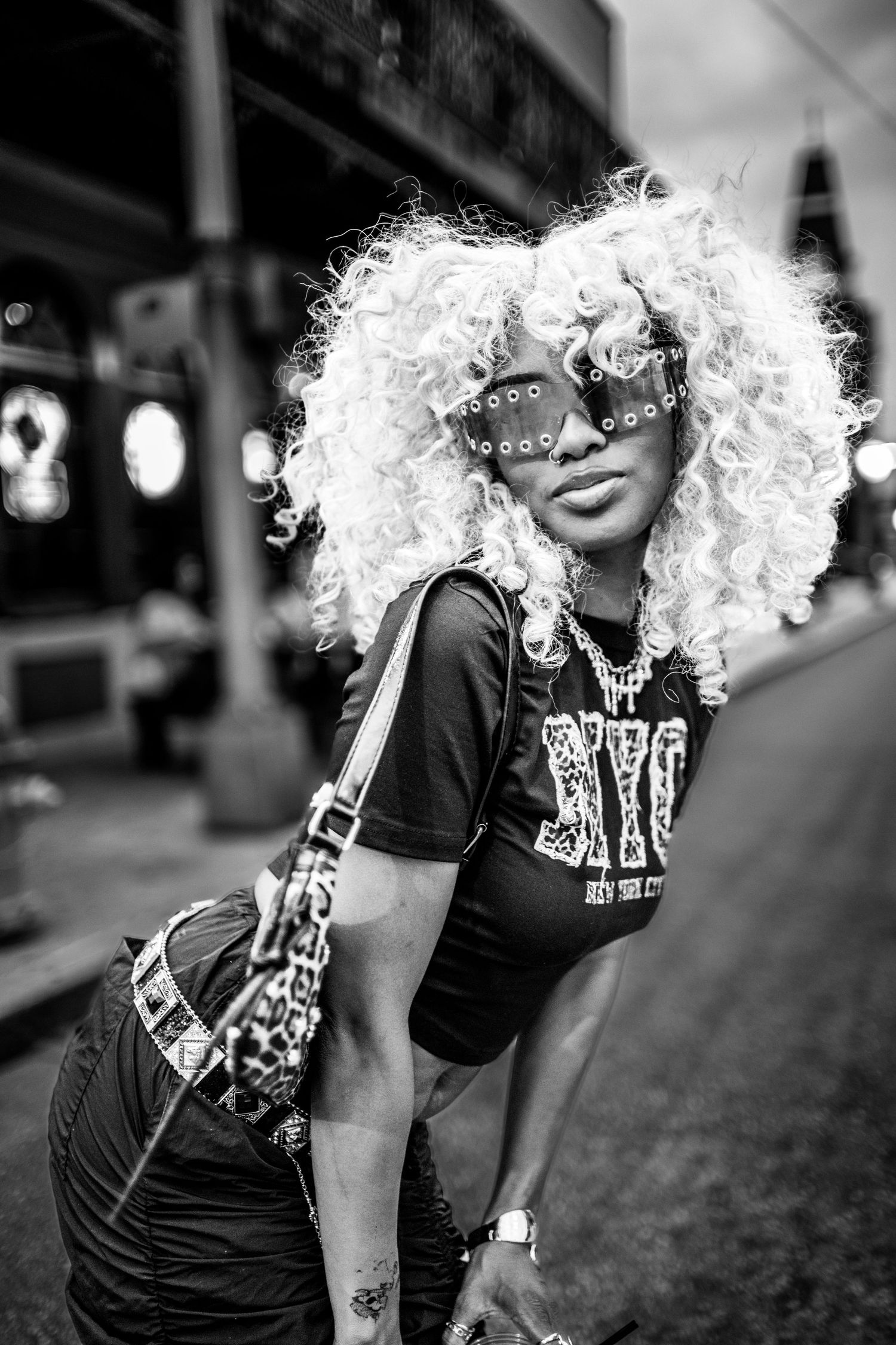 Black and white photo series of a person with curly blonde wig posing playfully on an urban street.
