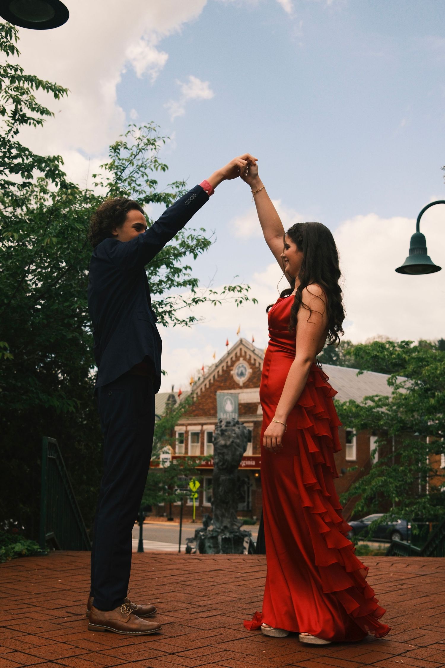 Dancing figures in formal wear twirl and pose dramatically on a brick courtyard with buildings in the background.