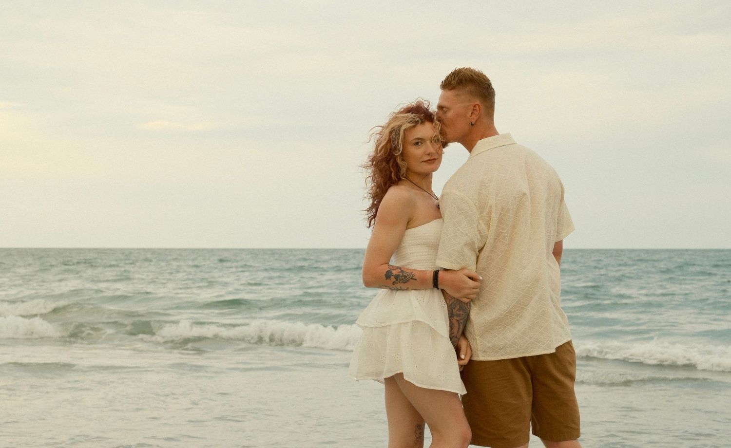 A couple embraces on a beach at sunset in a romantic photoshoot series.