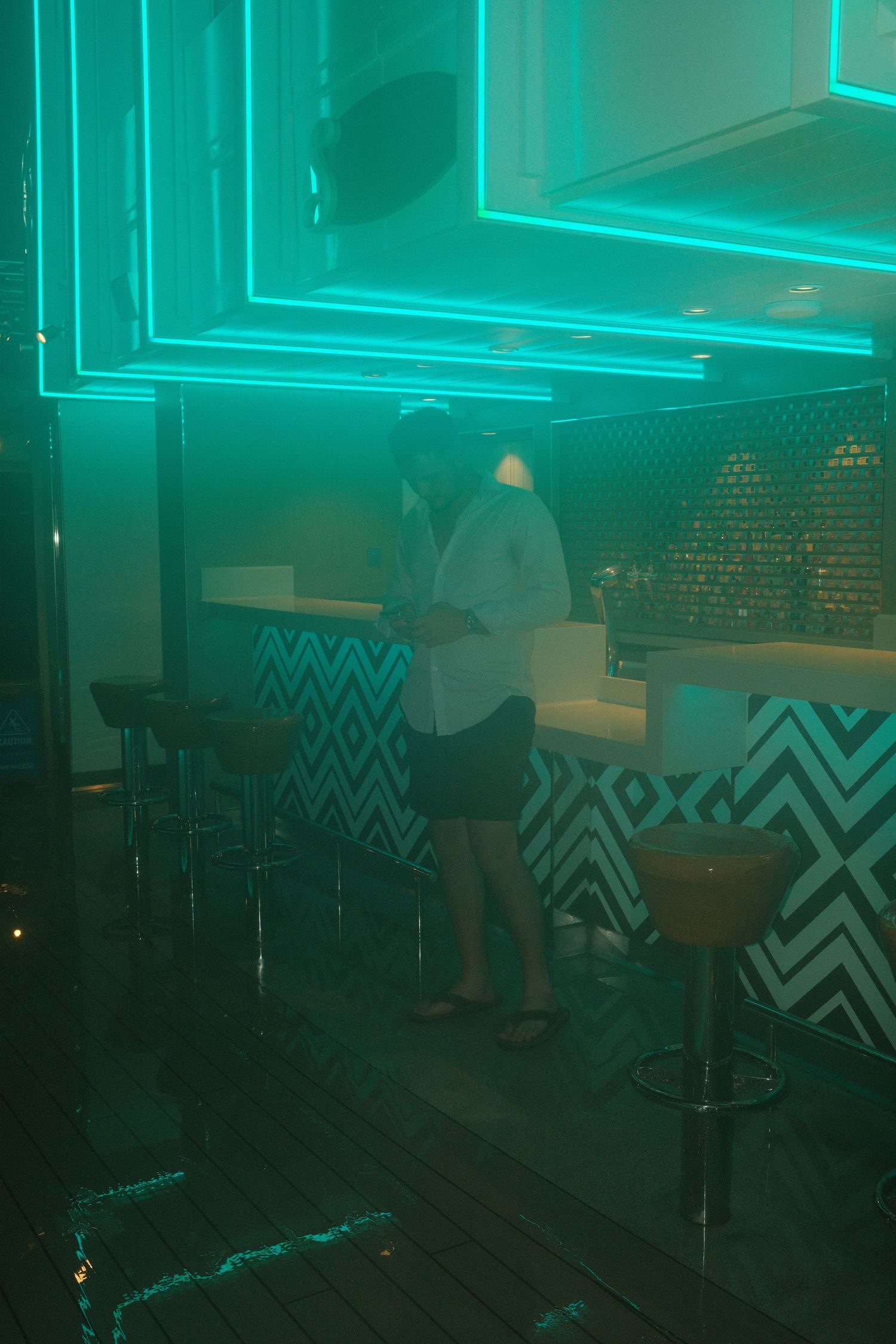 Nightclub interior bathed in neon turquoise lighting with geometric patterns on the walls.