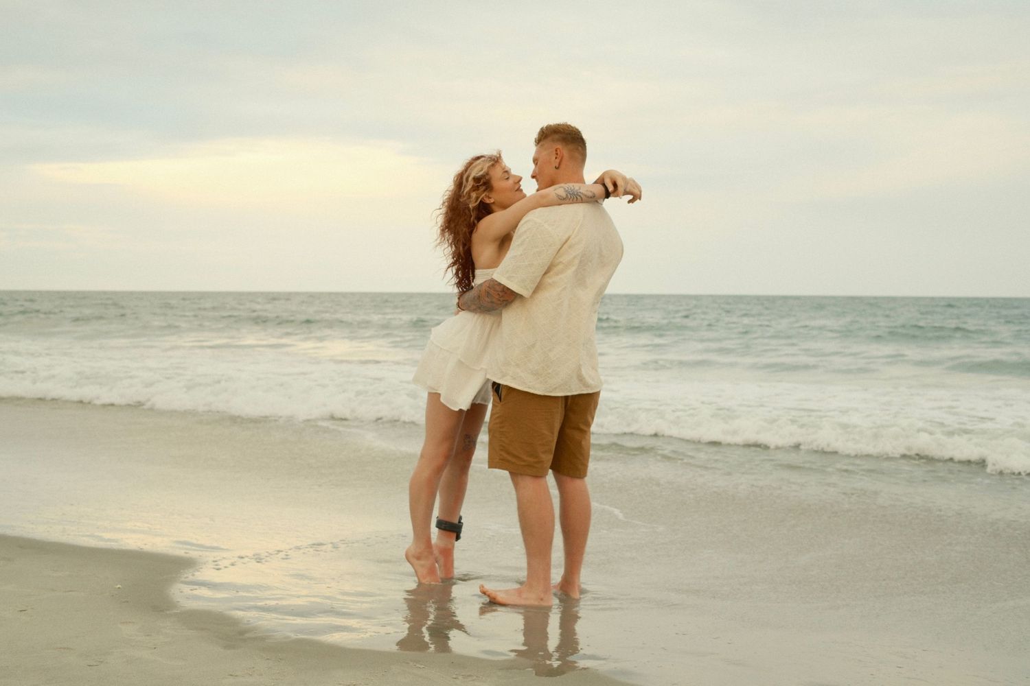 Romantic couple sharing intimate moments on a serene beach at sunset.