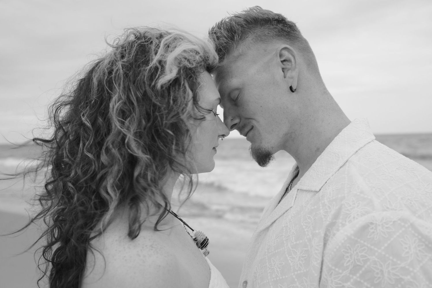 A romantic black and white photo series of a couple embracing on the beach at sunset.