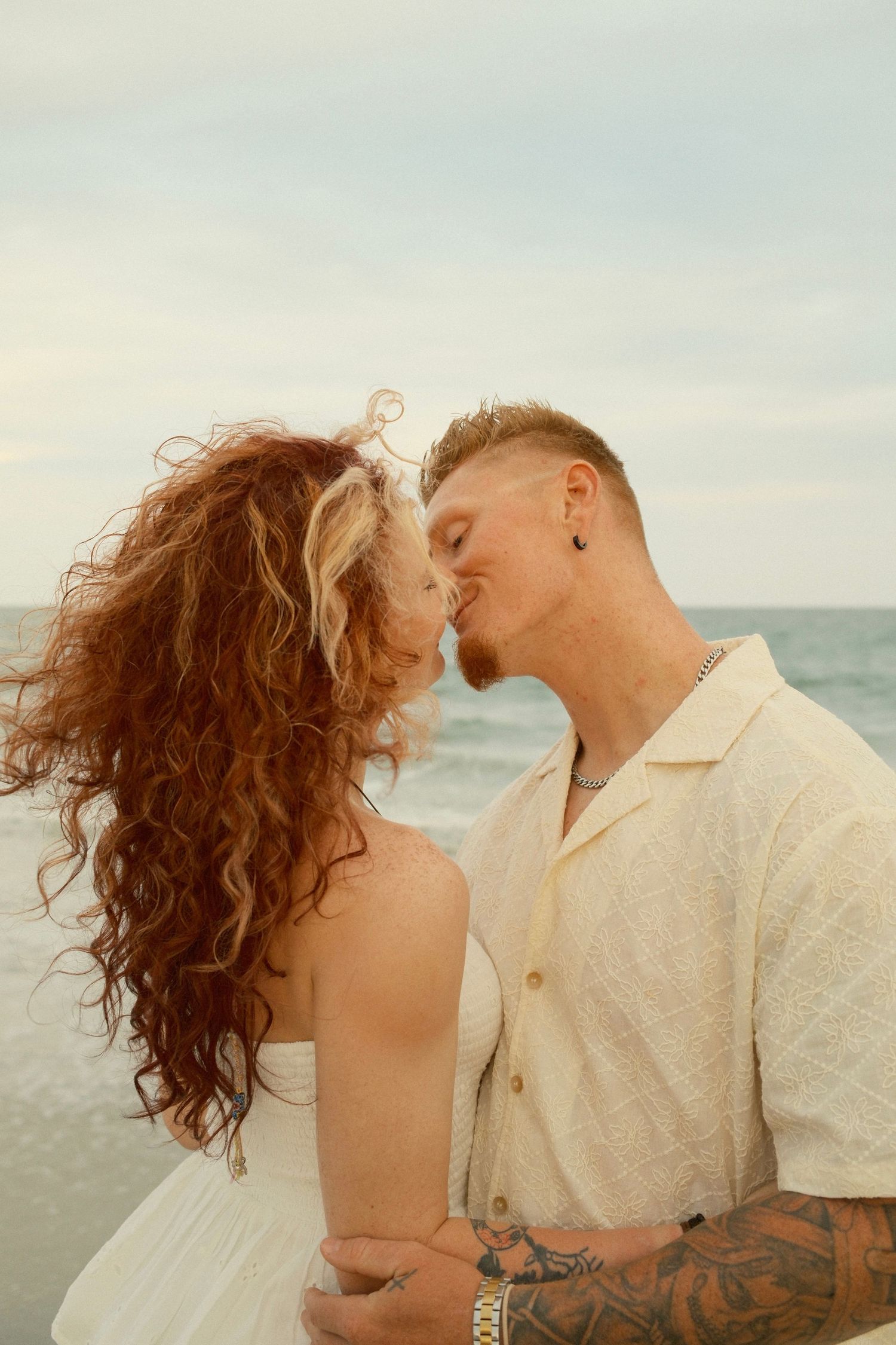 An intimate moment between a couple on the beach with waves and sunset in the background.