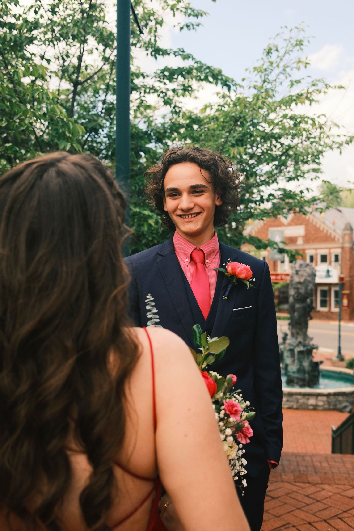 A couple in formal attire with a navy suit and red tie pose together on brick steps outdoors.
