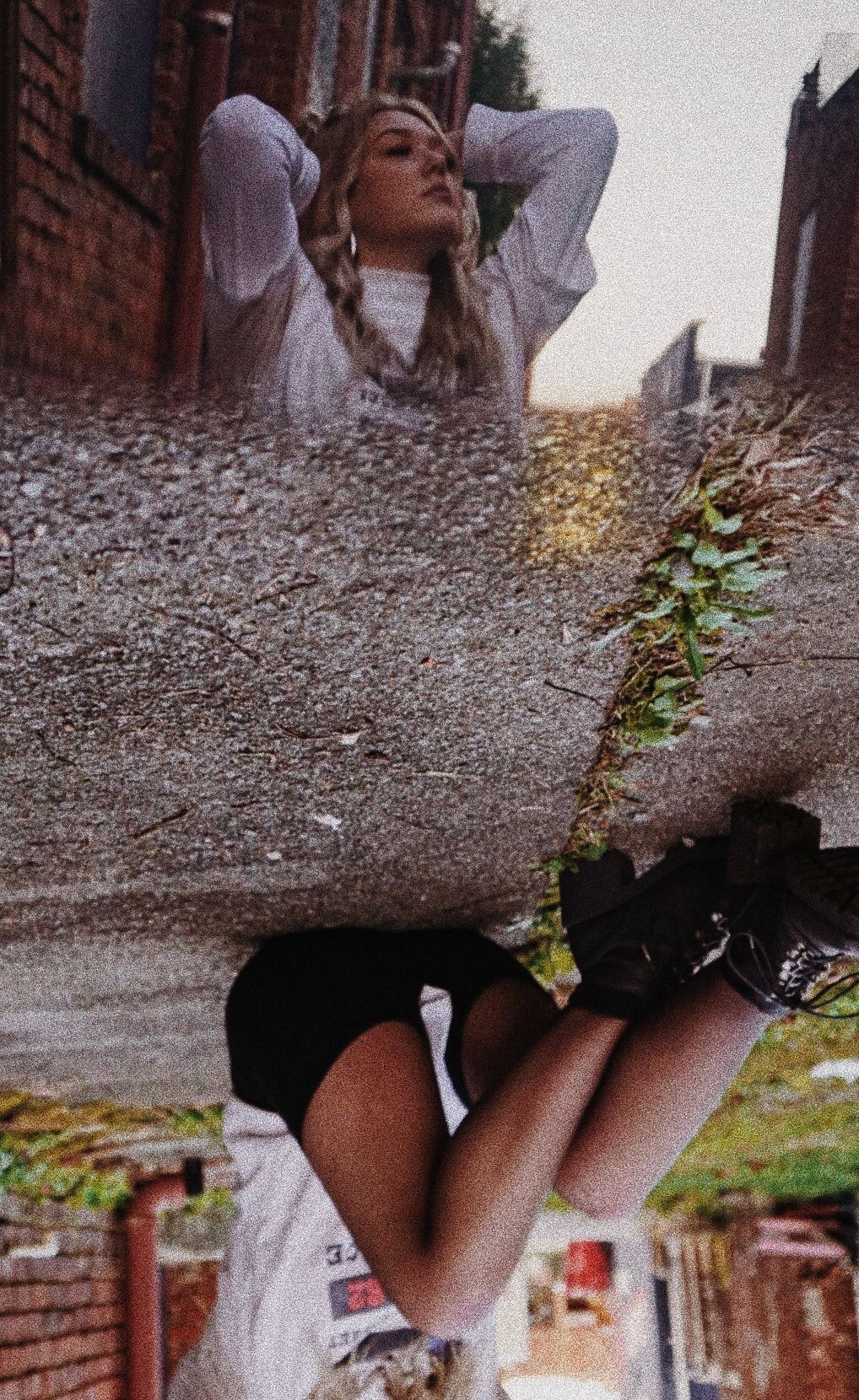 Artistic double exposure photo showing a person in white sweater against brick wall with upside-down urban scenery.