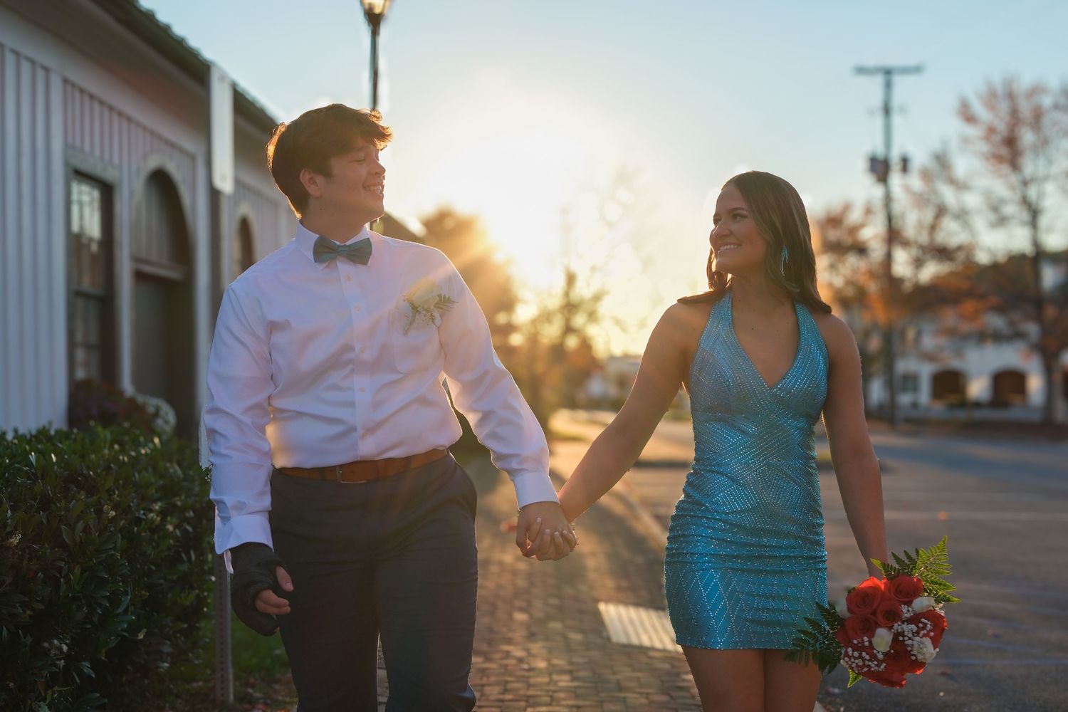 Couple holding hands and walking together at sunset with lens flare in an urban setting.