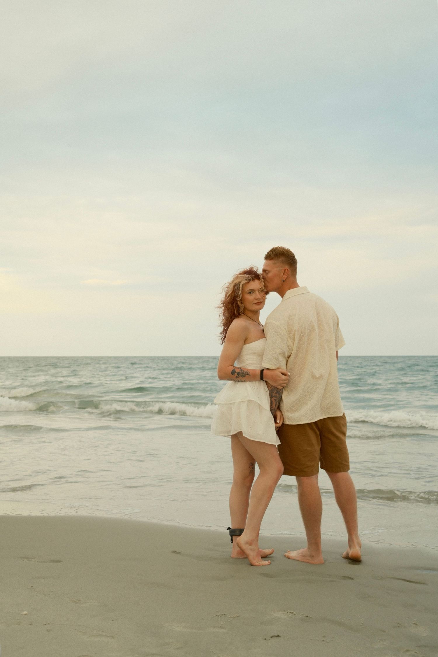A couple shares a romantic moment while walking together on a sandy beach at sunset.