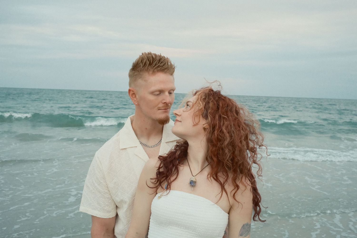 A loving couple shares romantic moments on a beach with turquoise waters in the background.