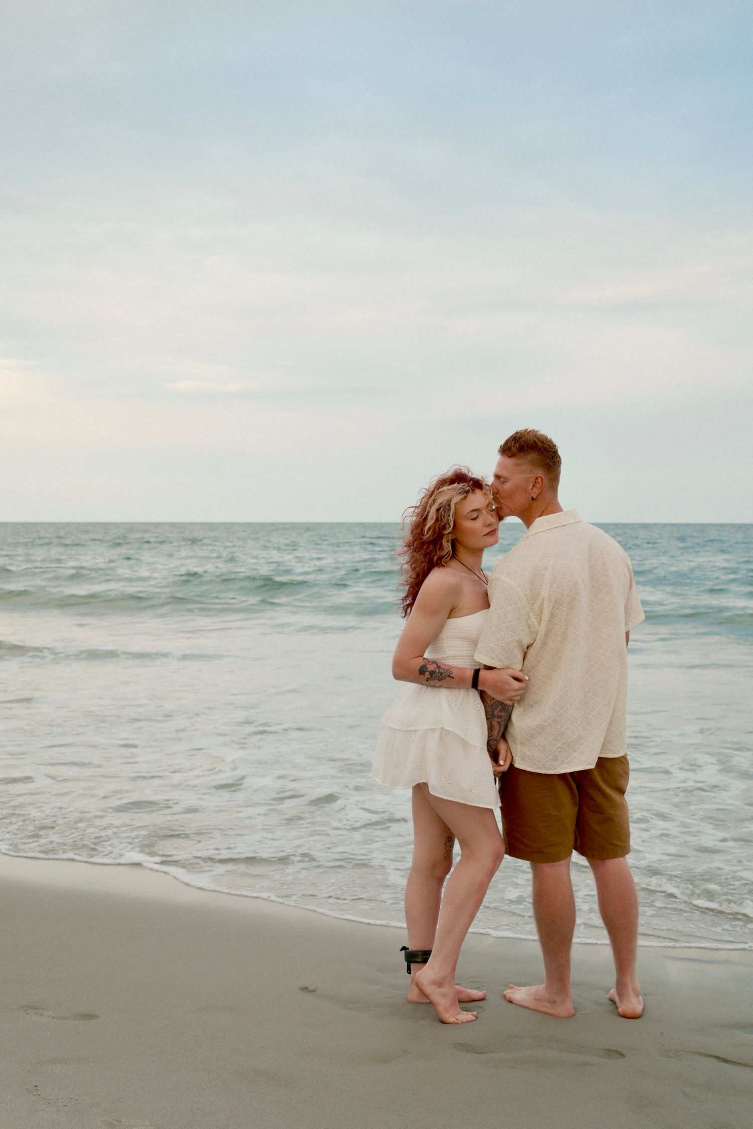 A couple shares romantic moments together walking along a serene beach at sunset.