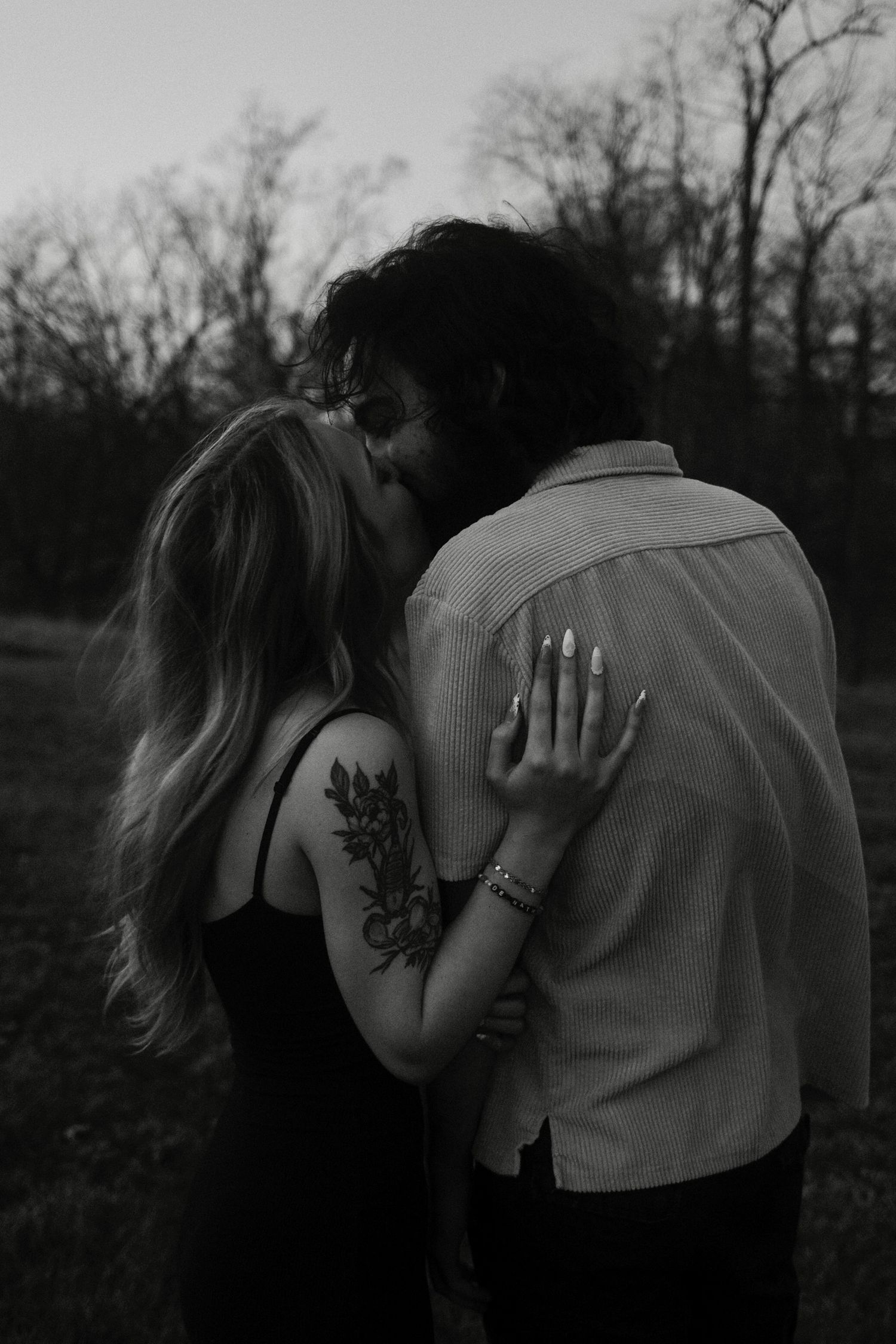 Black and white romantic photo of a couple embracing outdoors, with the woman showing a floral tattoo on her arm.