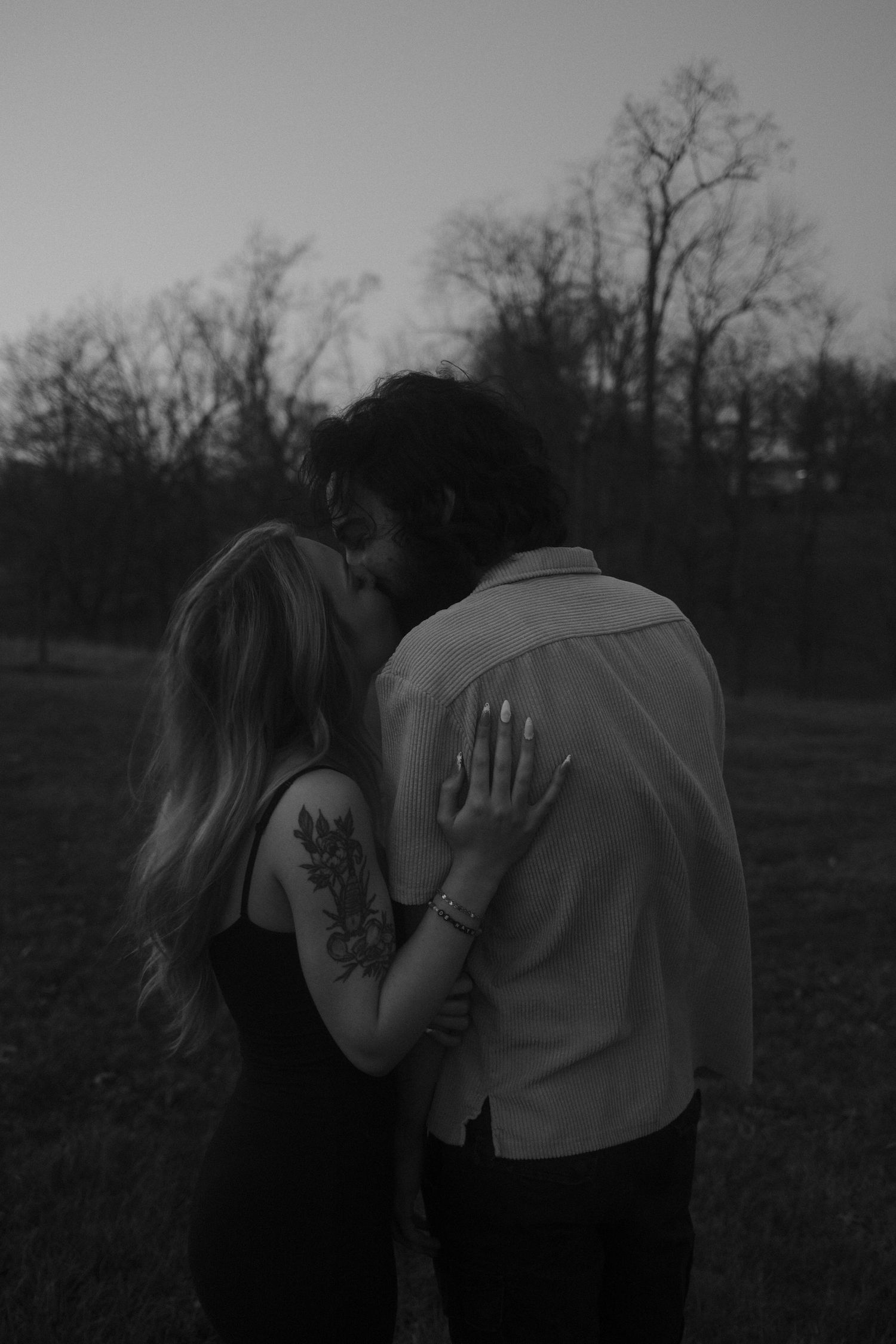 A romantic black and white photo of a couple embracing outdoors with bare trees in the background.