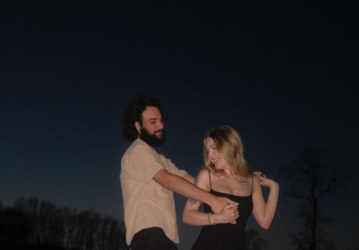 A couple dances together in silhouette against a dark background during sunset.