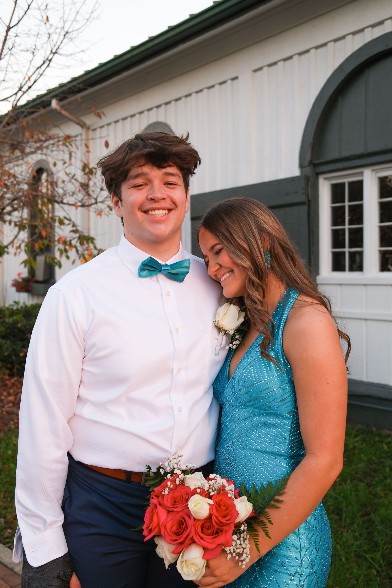 A formal couple shares a romantic moment in front of a white building with a turquoise dress and bow tie.
