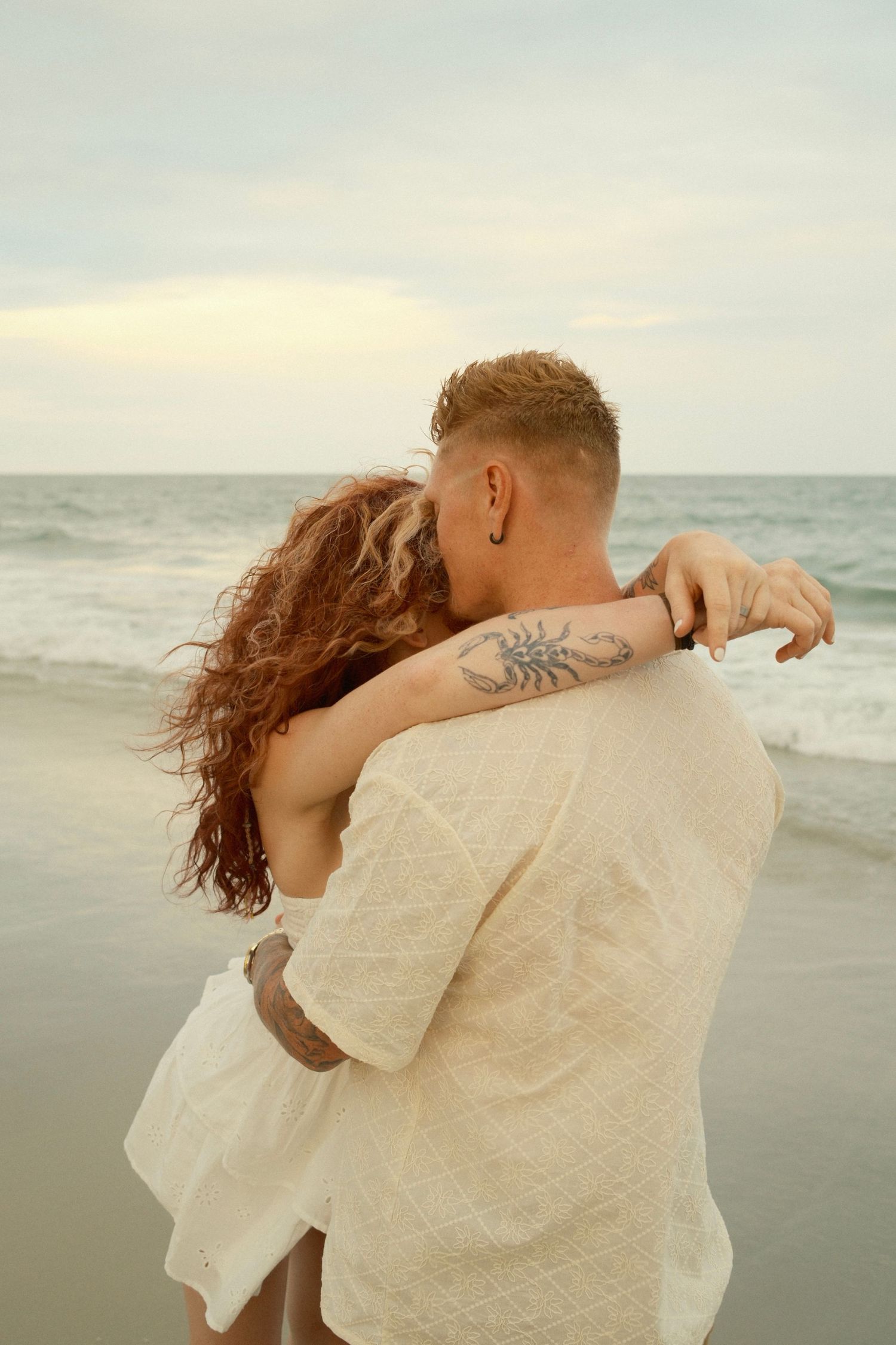 A romantic couple embraces on a misty beach at sunset, their silhouettes merging against the ocean backdrop.