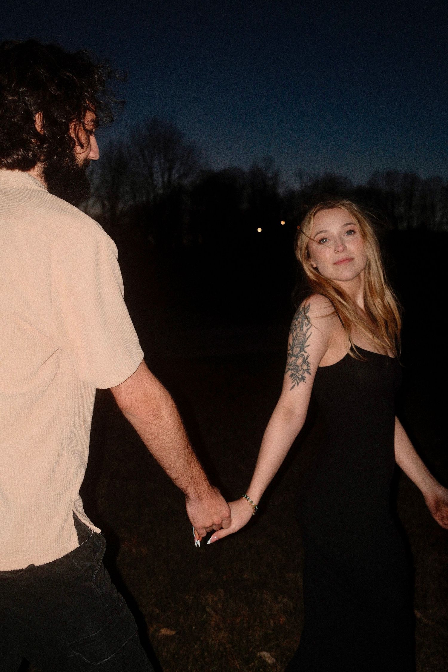 A couple poses together in silhouette against a dark evening sky in a romantic outdoor setting.