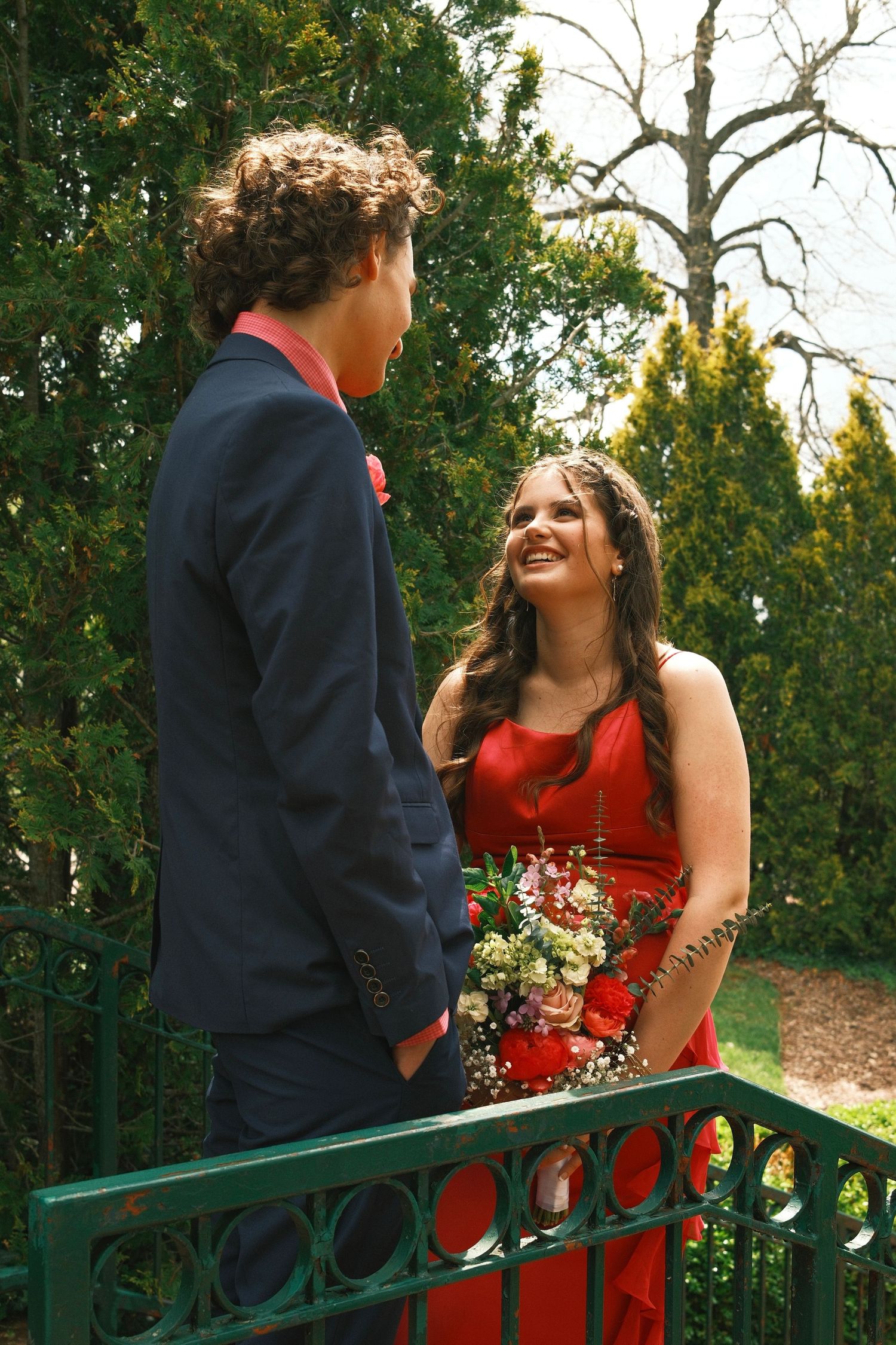 A couple laughs together while standing by a decorative metal railing in a garden setting.